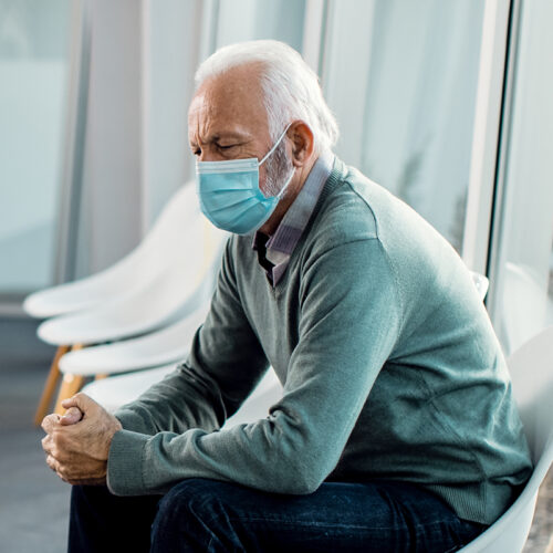 Pensive senior man with protective face mask sitting in waiting room at the hospital.