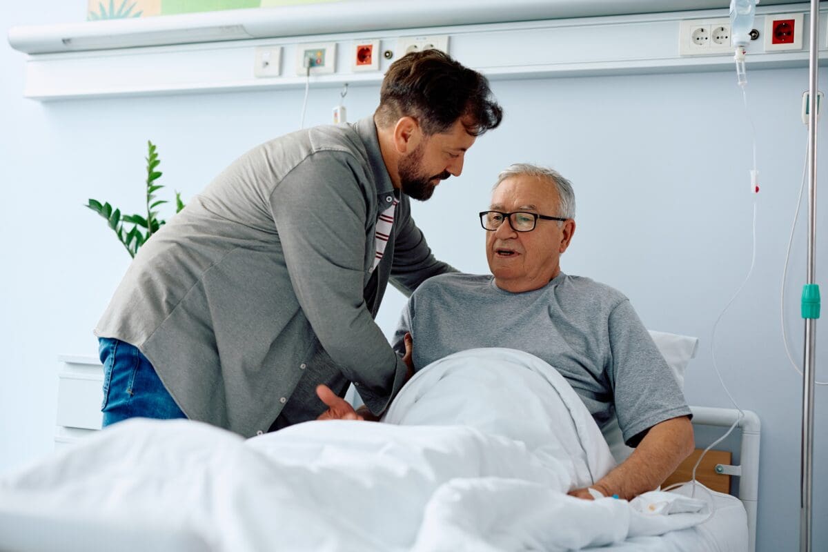 adult son helping senior father in hospital bed