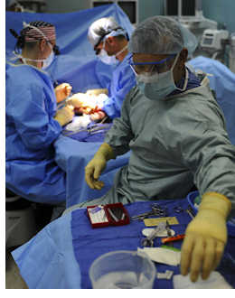 3 surgeons in PPE attend a patient undergoing a procedure in a surgical setting