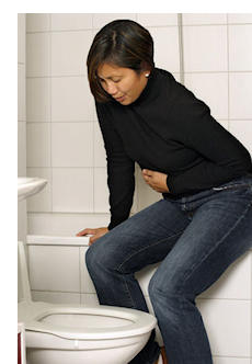 Editorial Photo: A clothed women in a bathroom stall winces and stands hunched over in pain